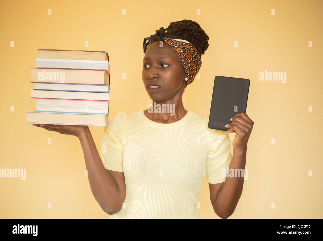 giovane donna che confronta libri stampati con e-book mentre accigliava a libri sulla sua mano destra e e-book sulla sua mano sinistra Foto Stock