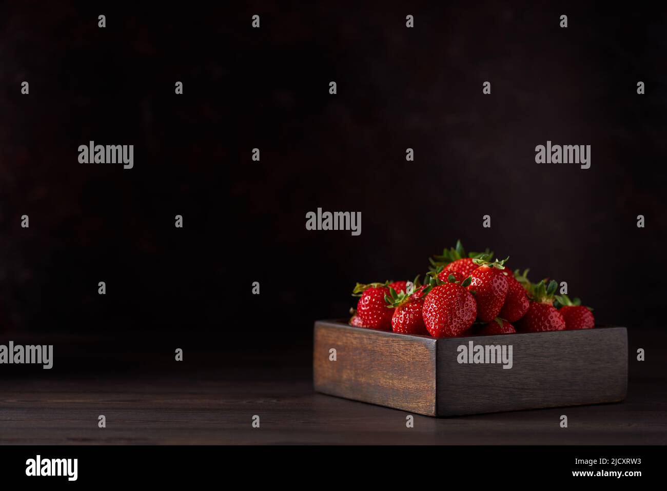 Fragole fresche in una ciotola di legno quadrata su un tavolo di legno marrone. Sfondo marrone. Primo piano, spazio di copia. Foto Stock