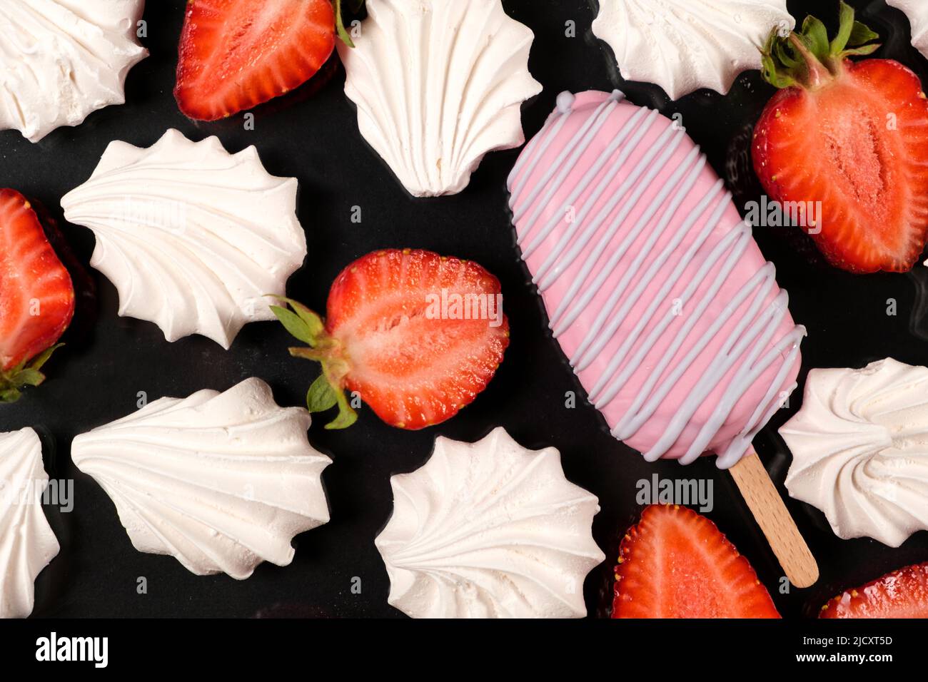 Gelato rosa su un bastone, meringa e fragole su sfondo nero. Foto Stock