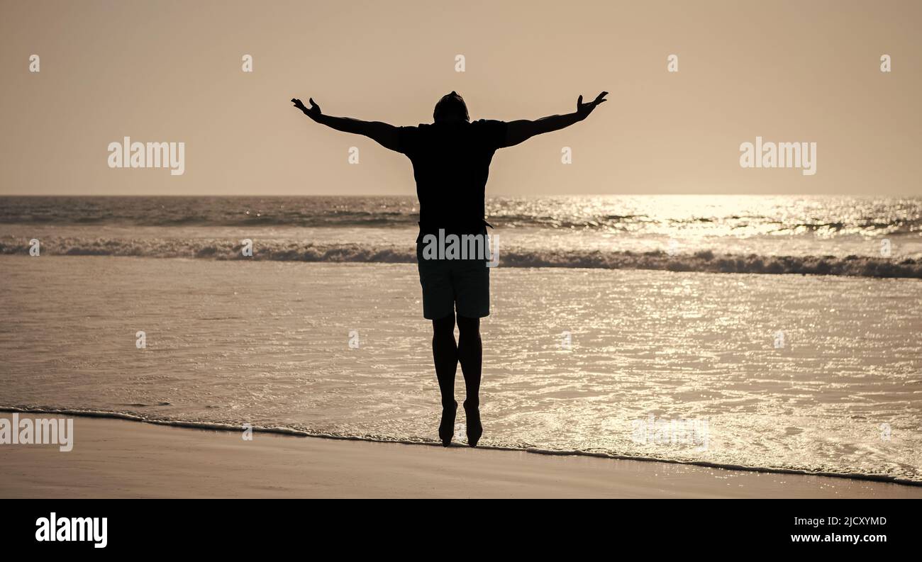 silhouette uomo sana, mani rialzate sulla spiaggia. estate energica. libertà. Foto Stock