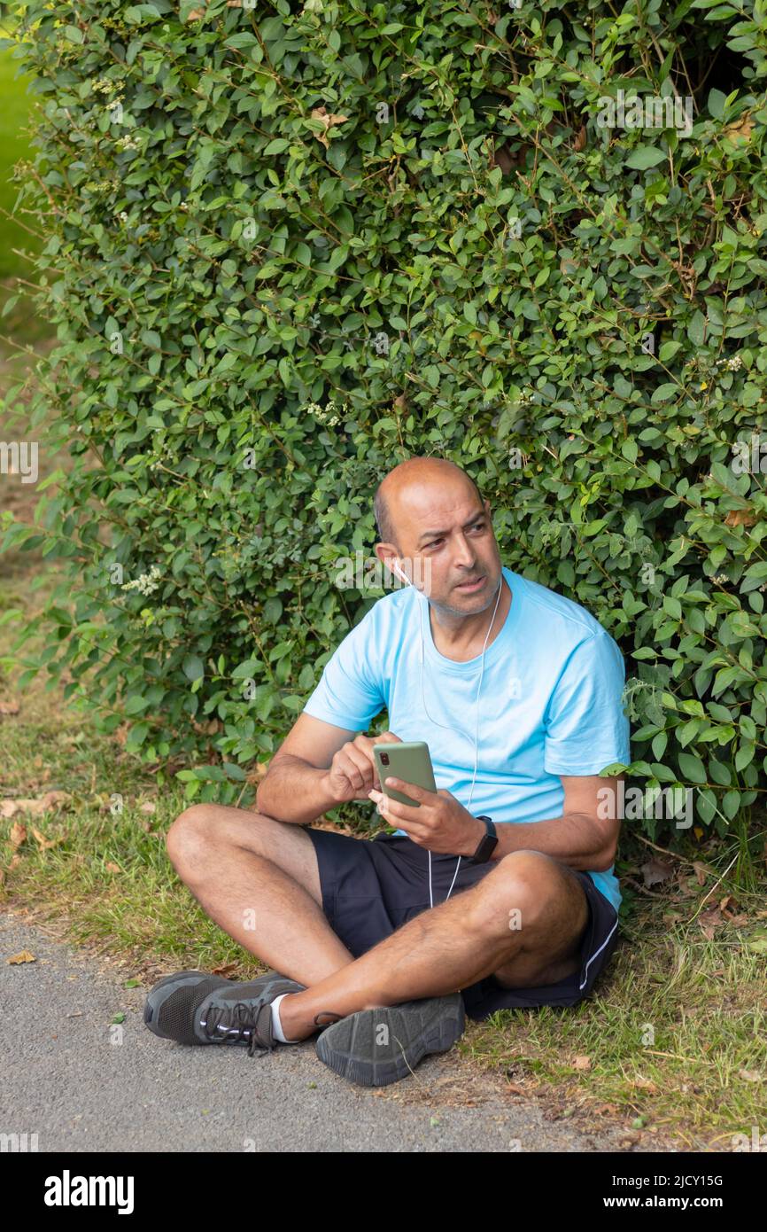 L'uomo calvo si stanca dopo una dura giornata di sport facendo una pausa per prendere il respiro mentre ascolta la musica Foto Stock