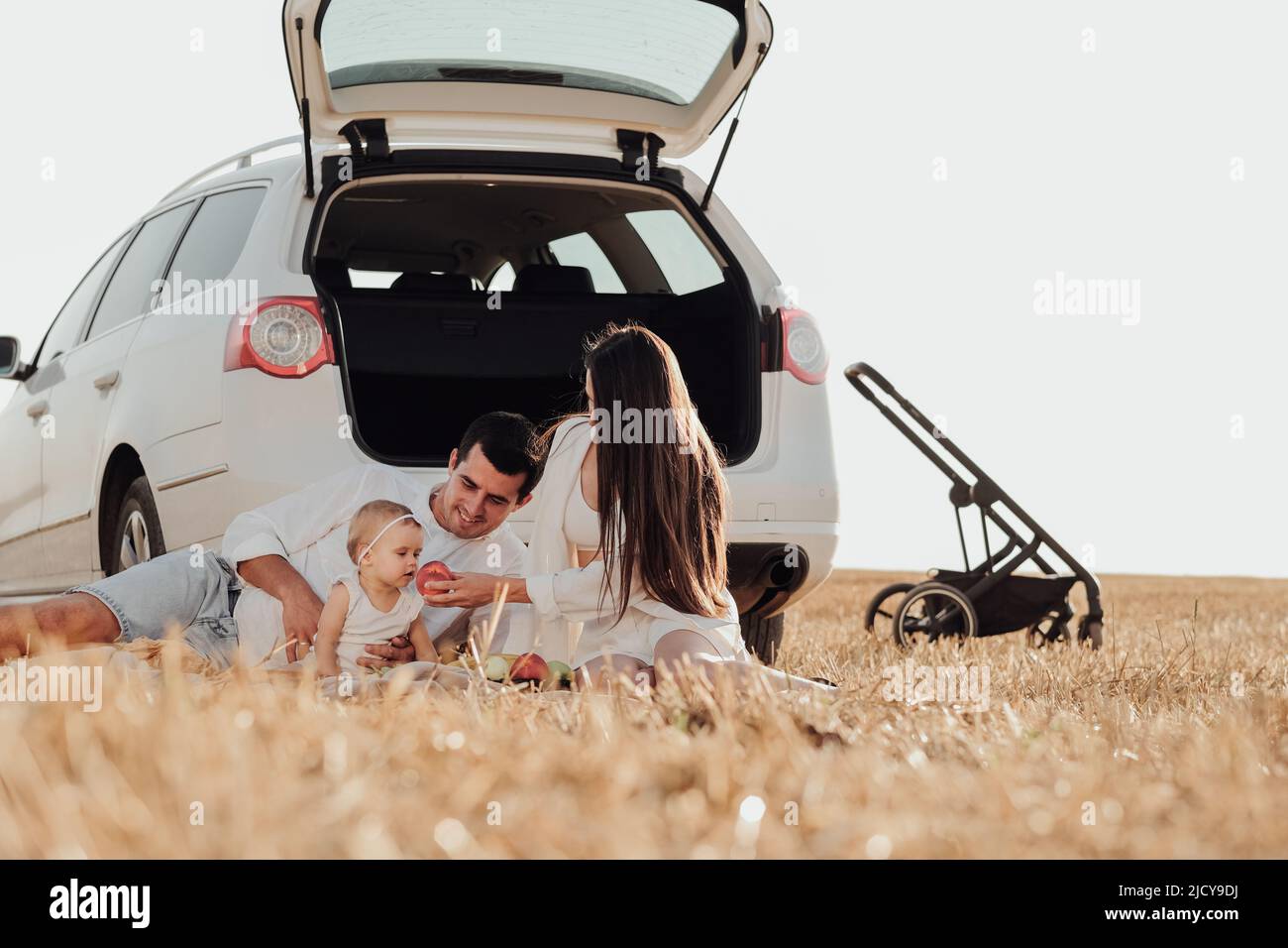 Famiglia giovane con bambino bambino che si gode picnic fuori della città, mamma e papà con loro figlia che hanno tempo di divertimento sul campo durante il Weekend Road Foto Stock
