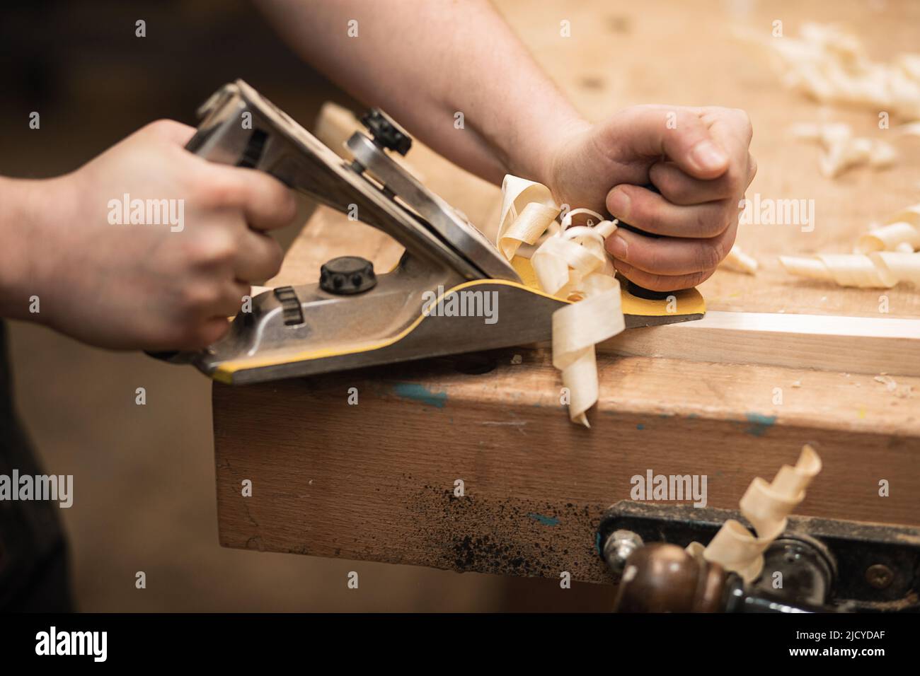 Primo piano delle mani del carpentiere tagliate che lavorano con l'attrezzatura dell'aereo sul banco da lavoro. Piallatrice per carpenteria in officina Foto Stock