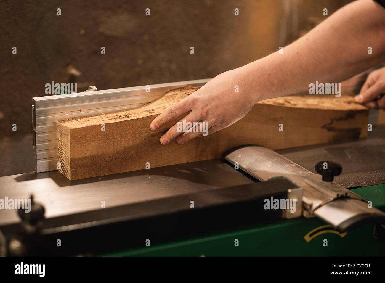 Primo piano delle mani di lavoro del carpentiere che fissano la barra di legno, il legno e il lavoro preciso con la macchina per il taglio del legno in officina Foto Stock