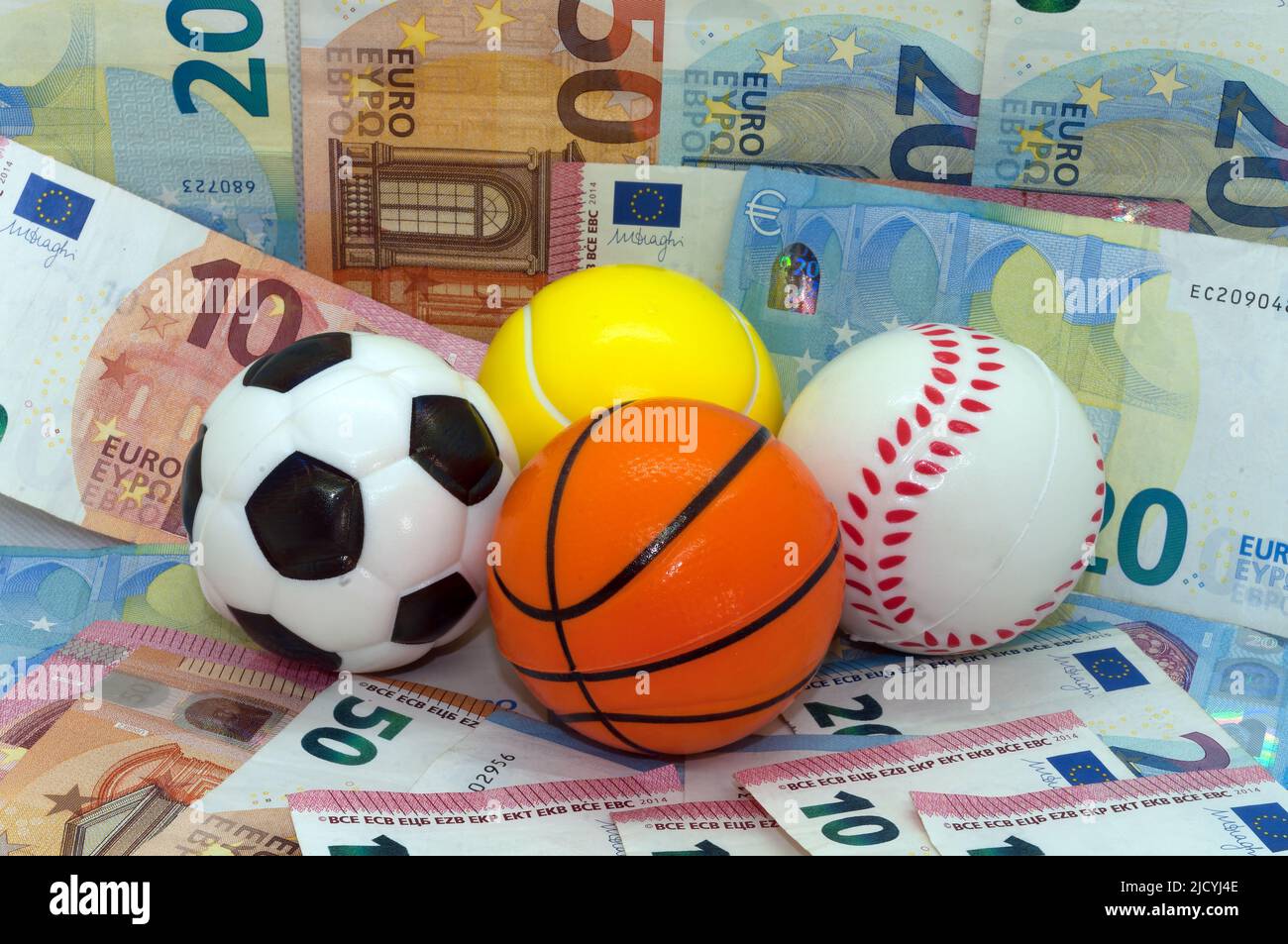 Immagine simbolo: sport e denaro, palline su sfondo di banconote Foto Stock