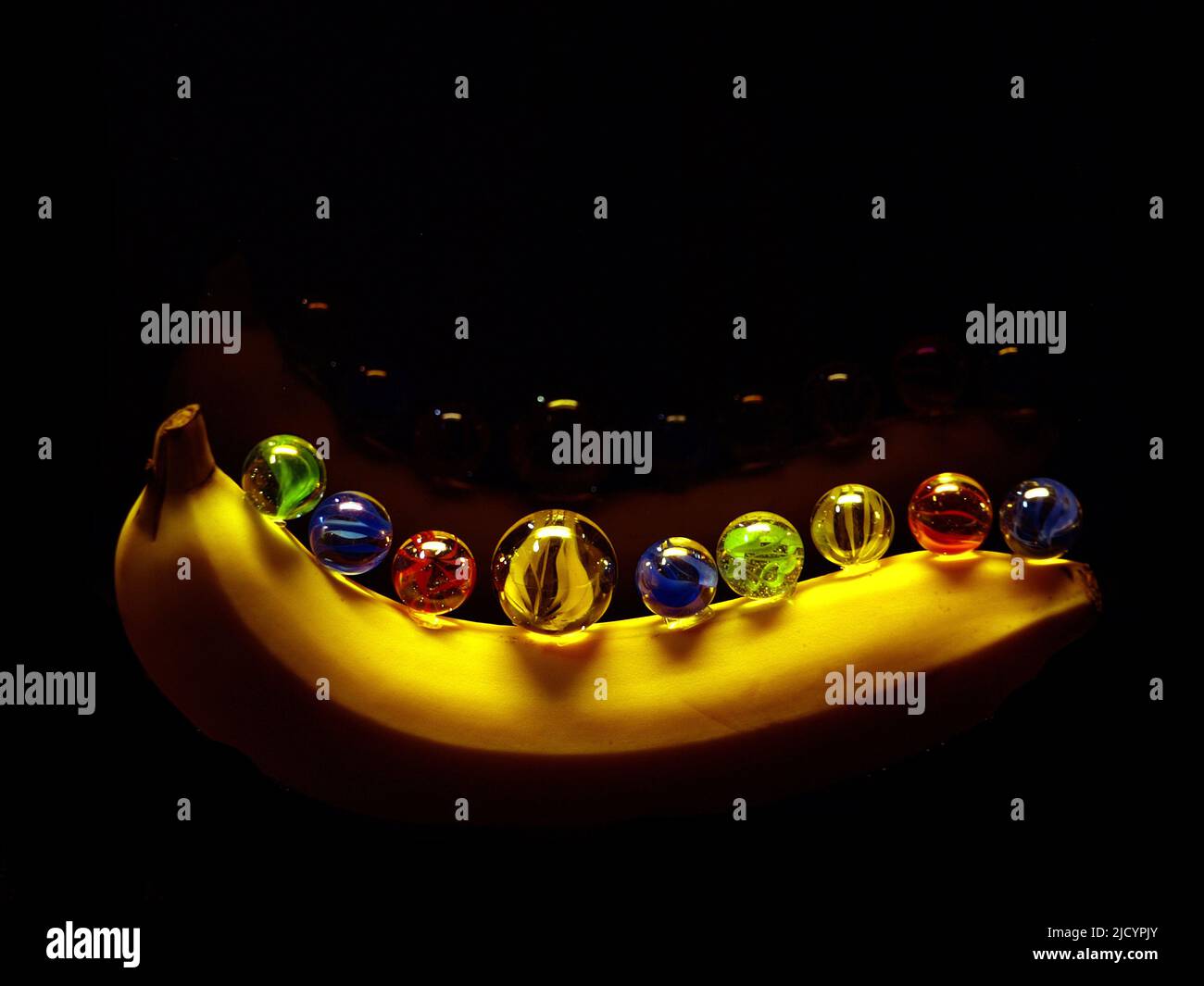Una banana fresca sulla parte superiore sono marmi colorati rivestiti riflessi in uno sfondo nero in un'illuminazione diretta a lunga esposizione scatto. Foto Stock