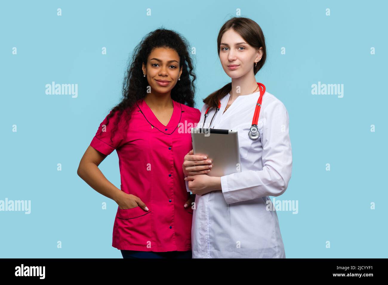 Donna caucasica Dottore con Tablet digitale e African American Female Nurse su sfondo Blue Studio. Diverse etnie Medical Team of Healthcare Foto Stock