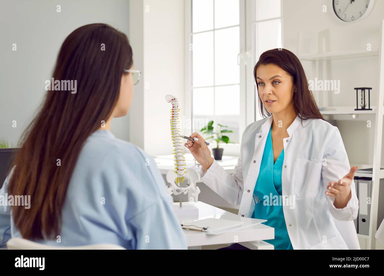 Il medico femminile che parla con il paziente indica le vertebre sul modello della colonna vertebrale indicando il principio del trattamento. Foto Stock