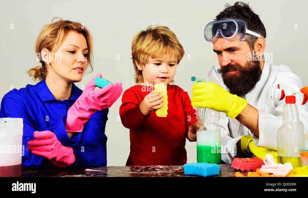 La famiglia pulisce insieme. Madre e padre insegnano al figlio piccolo pulire con spray detergente e spugna. Foto Stock