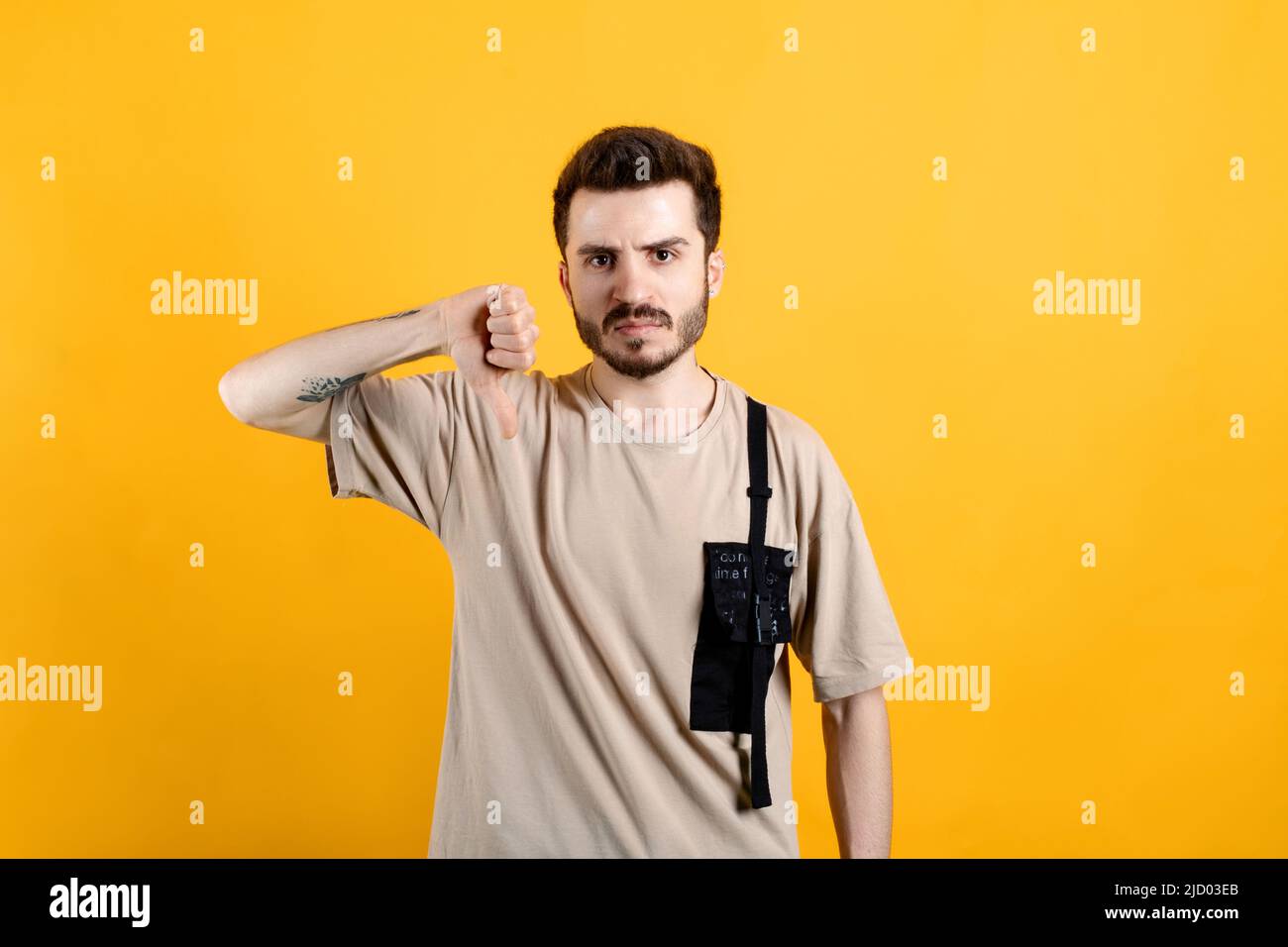 Giovane uomo caucasico che indossa una t-shirt in posa isolata su sfondo giallo che mostra il pollice verso il basso ed esprime inpiacere. Grumpy, insoddisfatto, infastidito, u Foto Stock