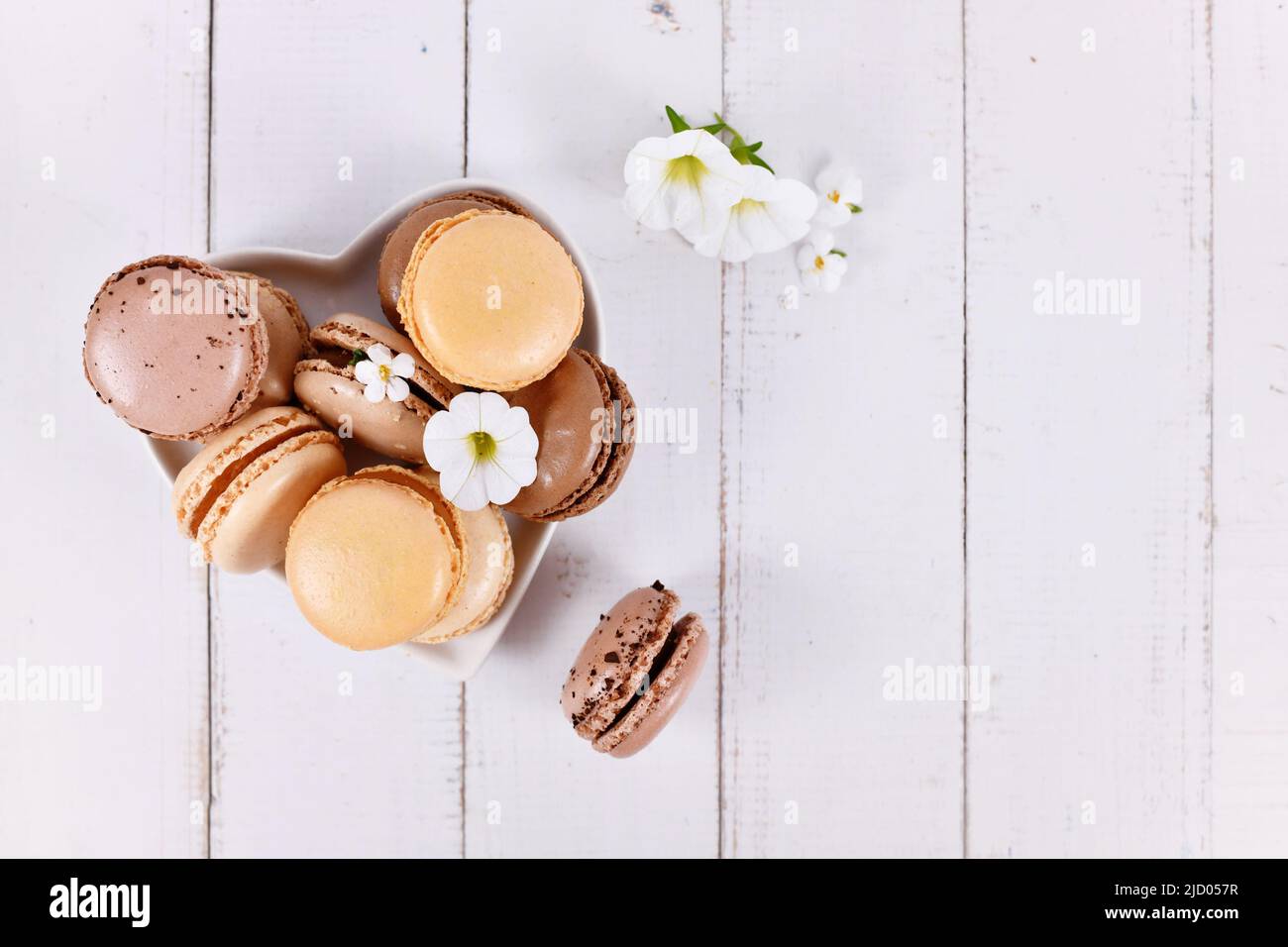 Macaron francese di colore marrone naturale, beige e crema su piatto a forma di cuore con spazio copia Foto Stock