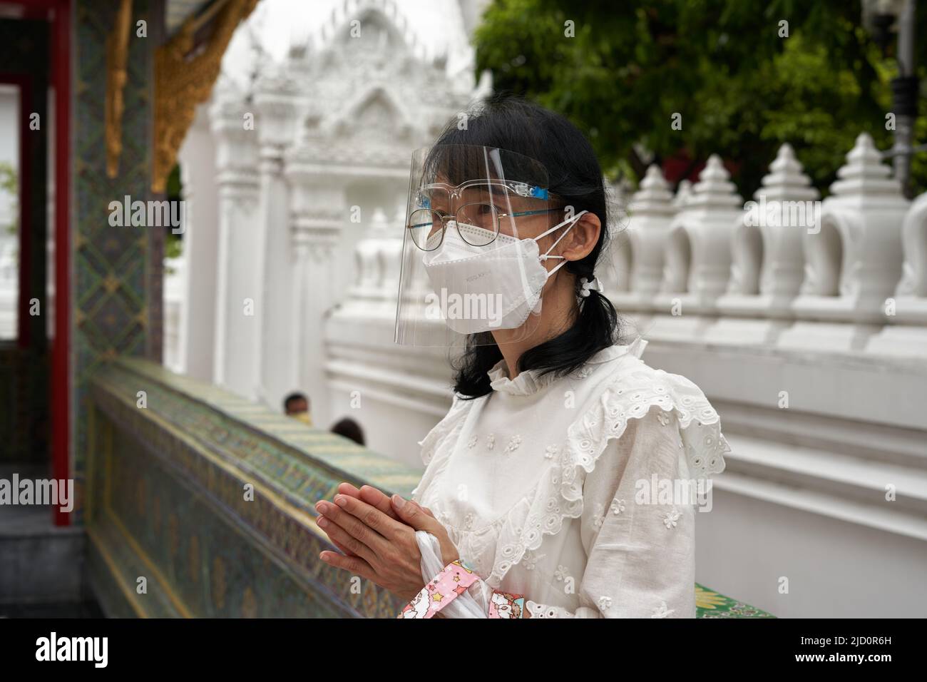 Bangkok, Thailandia, 16 febbraio 2022: Giovane donna con maschera di plastica covid facciale che prega in un tempio Foto Stock