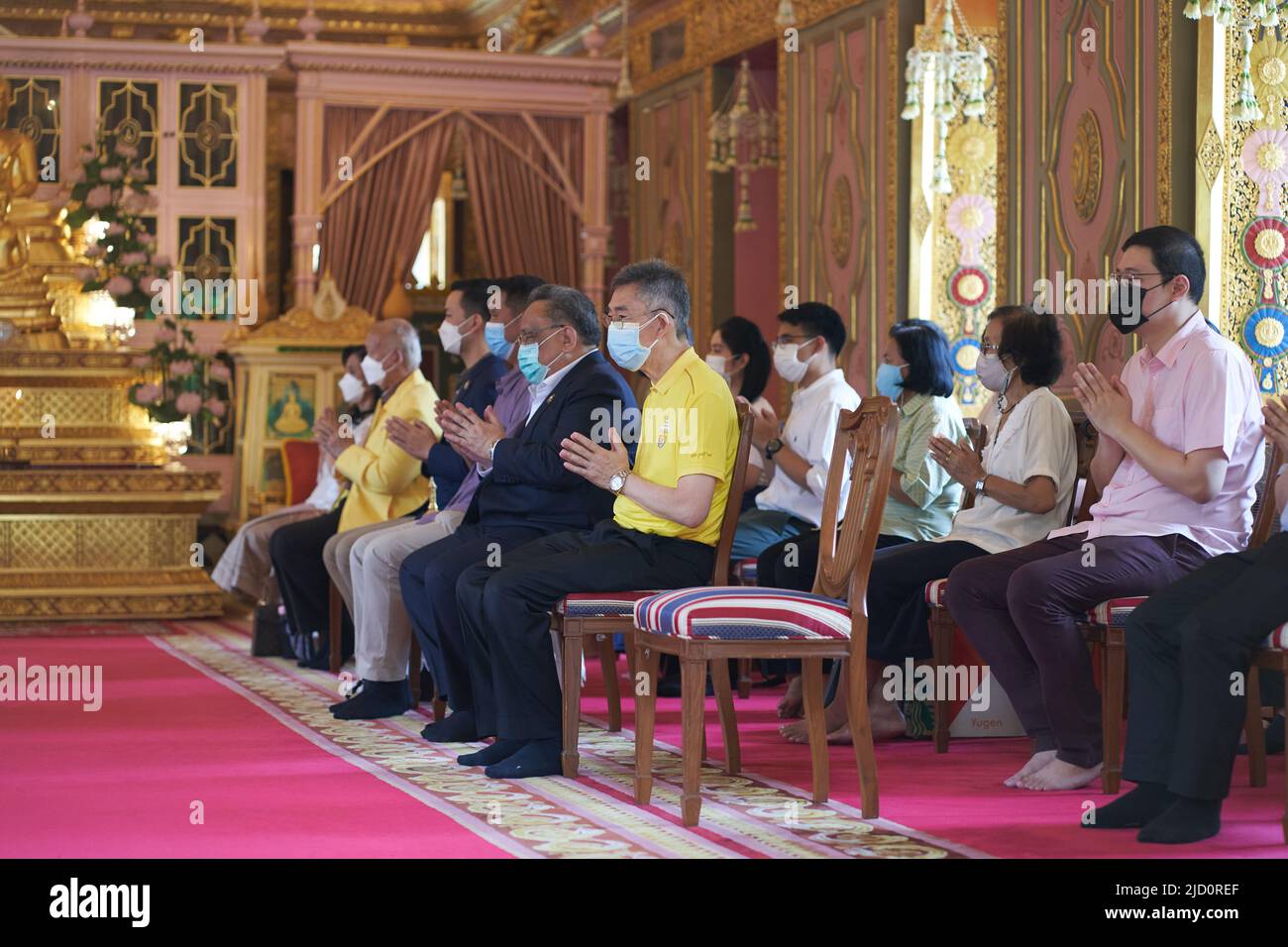 Bangkok, Thailandia, 16 febbraio 2022: Persone sedute su sedie all'interno di un tempio buddista mentre pregano Foto Stock