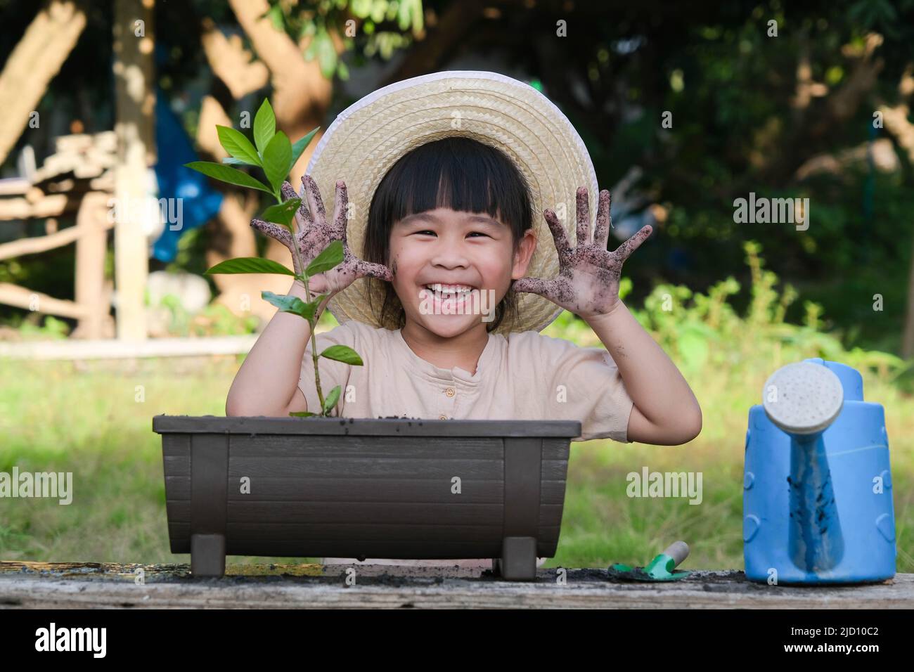 La bambina che indossa un cappello aiuta la madre nel giardino, un piccolo giardiniere. Cute ragazza piantando fiori in pentole. La ragazza piccola carina sorride e si mostra fuori Foto Stock