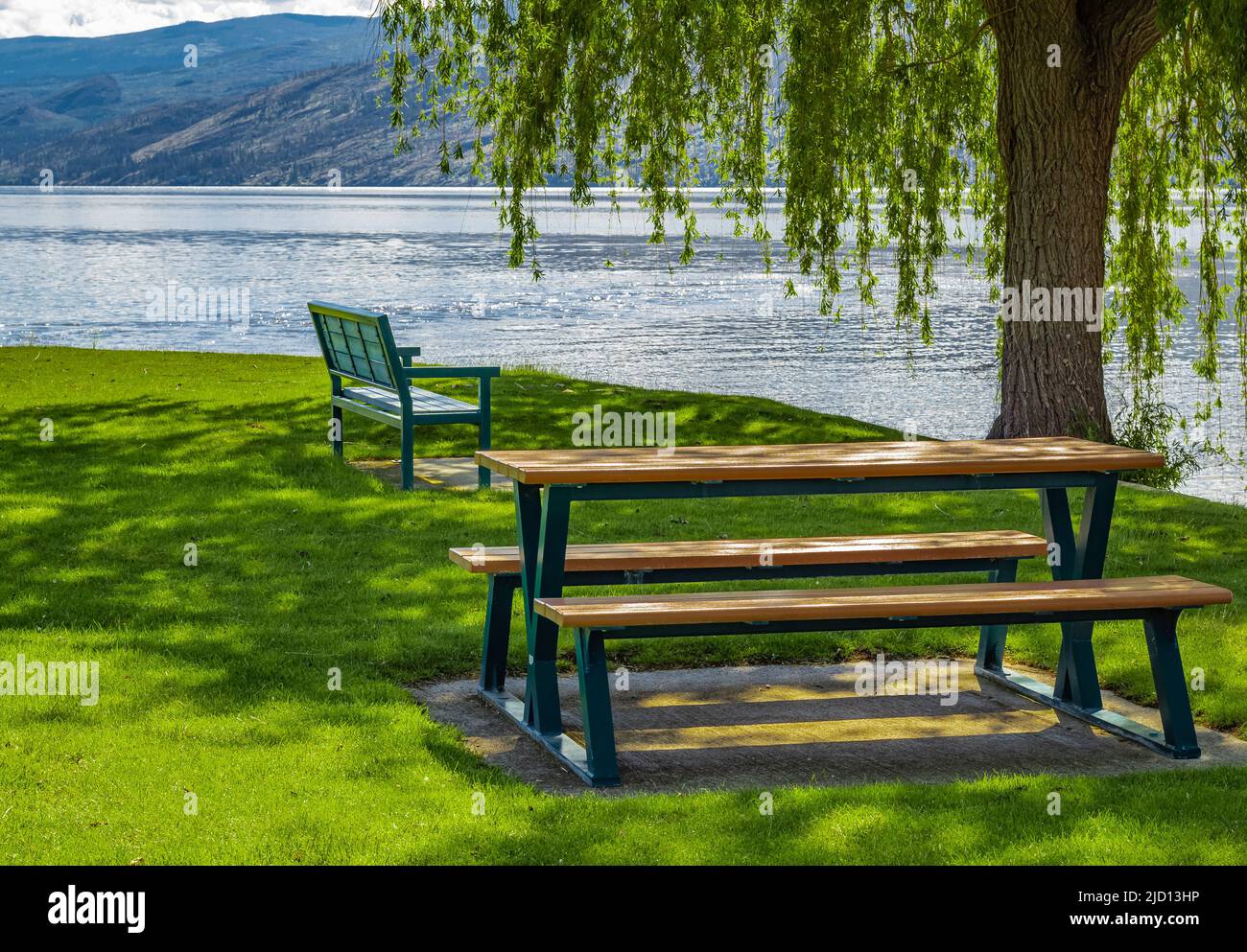 Tavolo vuoto in legno con sedie in un parco estivo al lago Okanagan BC Canada. Giornata calda di sole vicino al lago. Paesaggio alba mattina. Foto di viaggio, n Foto Stock