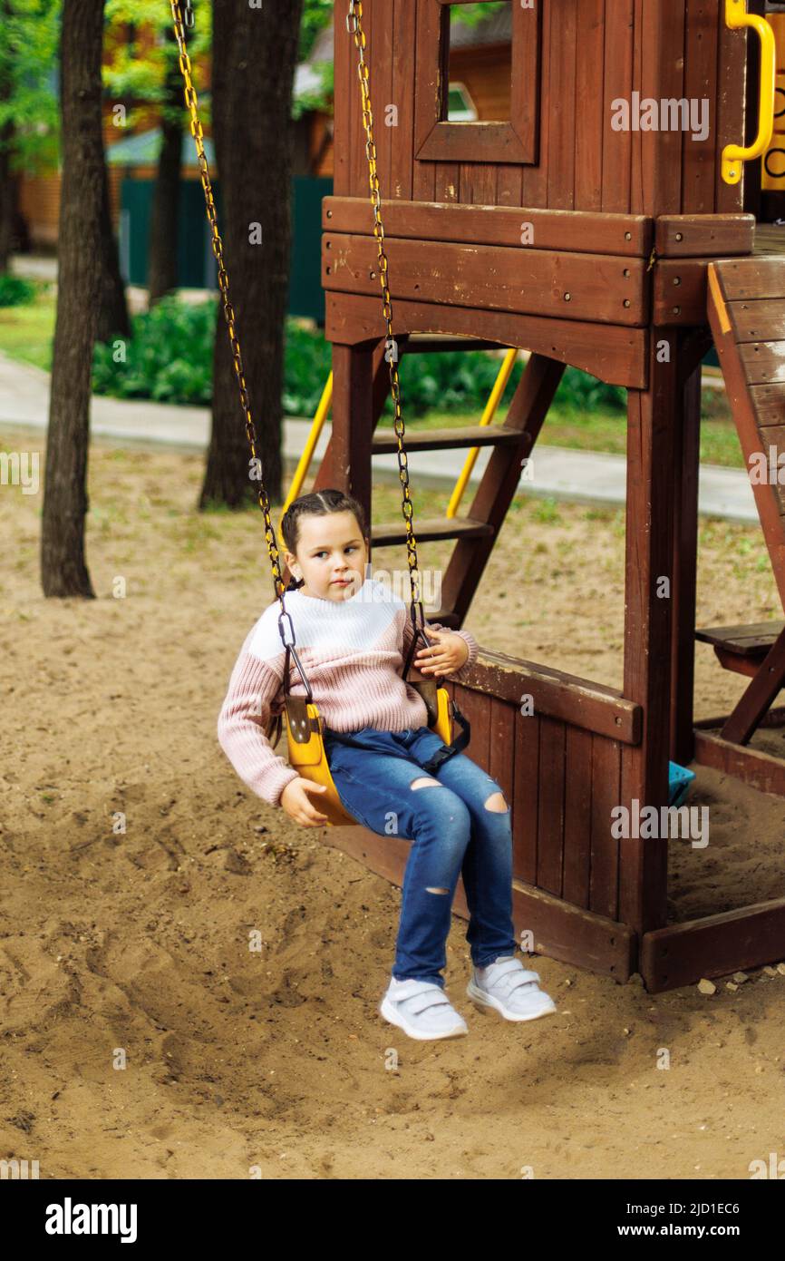 Carino ragazza piccola che brulica su swing giallo nel parco giochi in legno complesso di gioco. Vacanze estive in campeggio, centro turistico. Passeggiate e giochi all'aperto Foto Stock