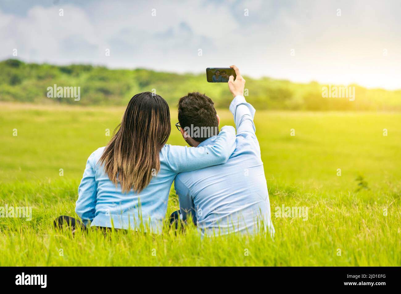 Giovane coppia innamorata che prende un selfie sul campo, gente innamorata che prende selfie sul campo con il loro smartphone, sorridente coppia innamorata seduta Foto Stock