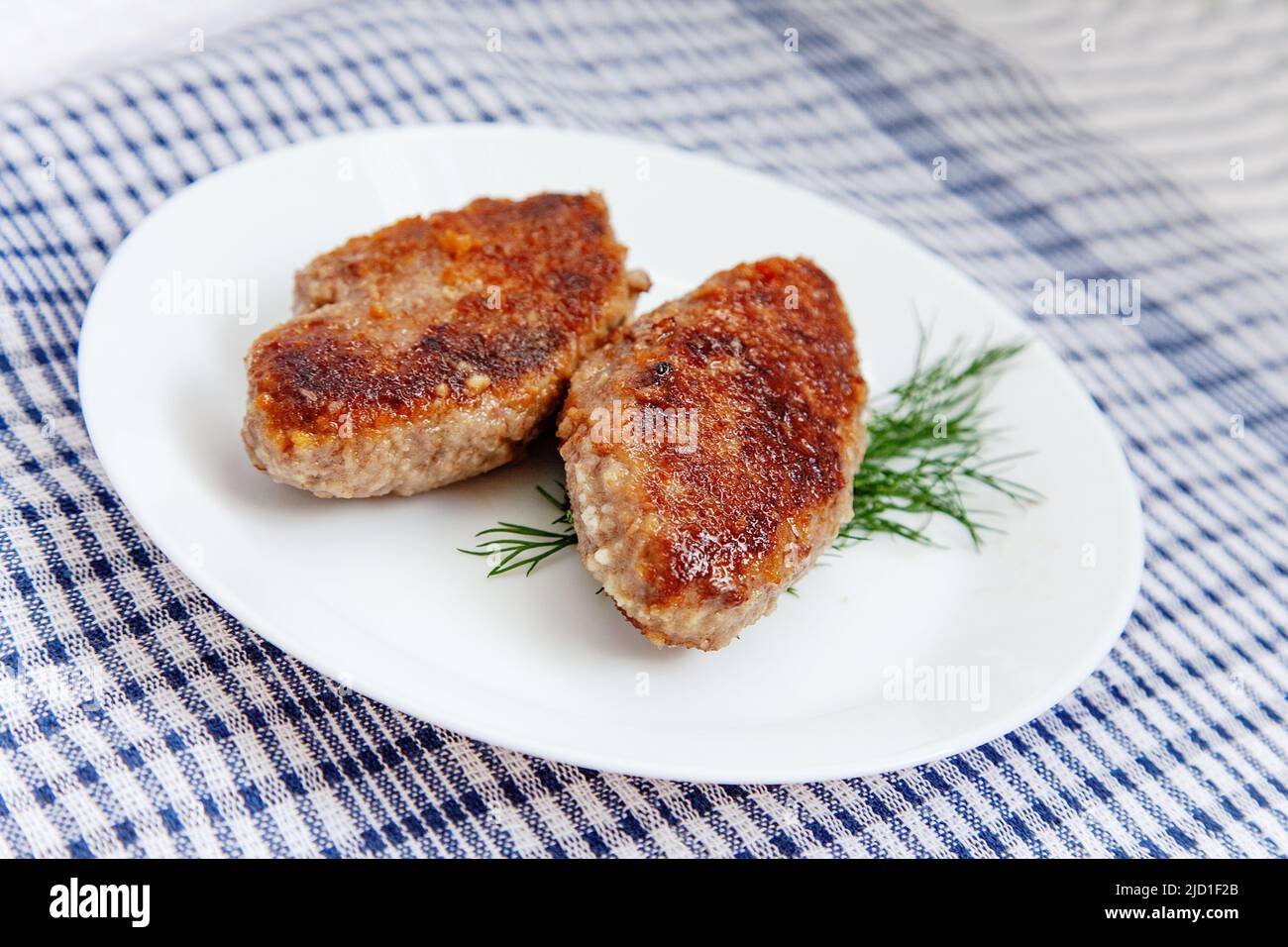 Piatto bianco con cotolette di manzo adagiato su tradizionale tovagliolo da cucina a pelo Foto Stock