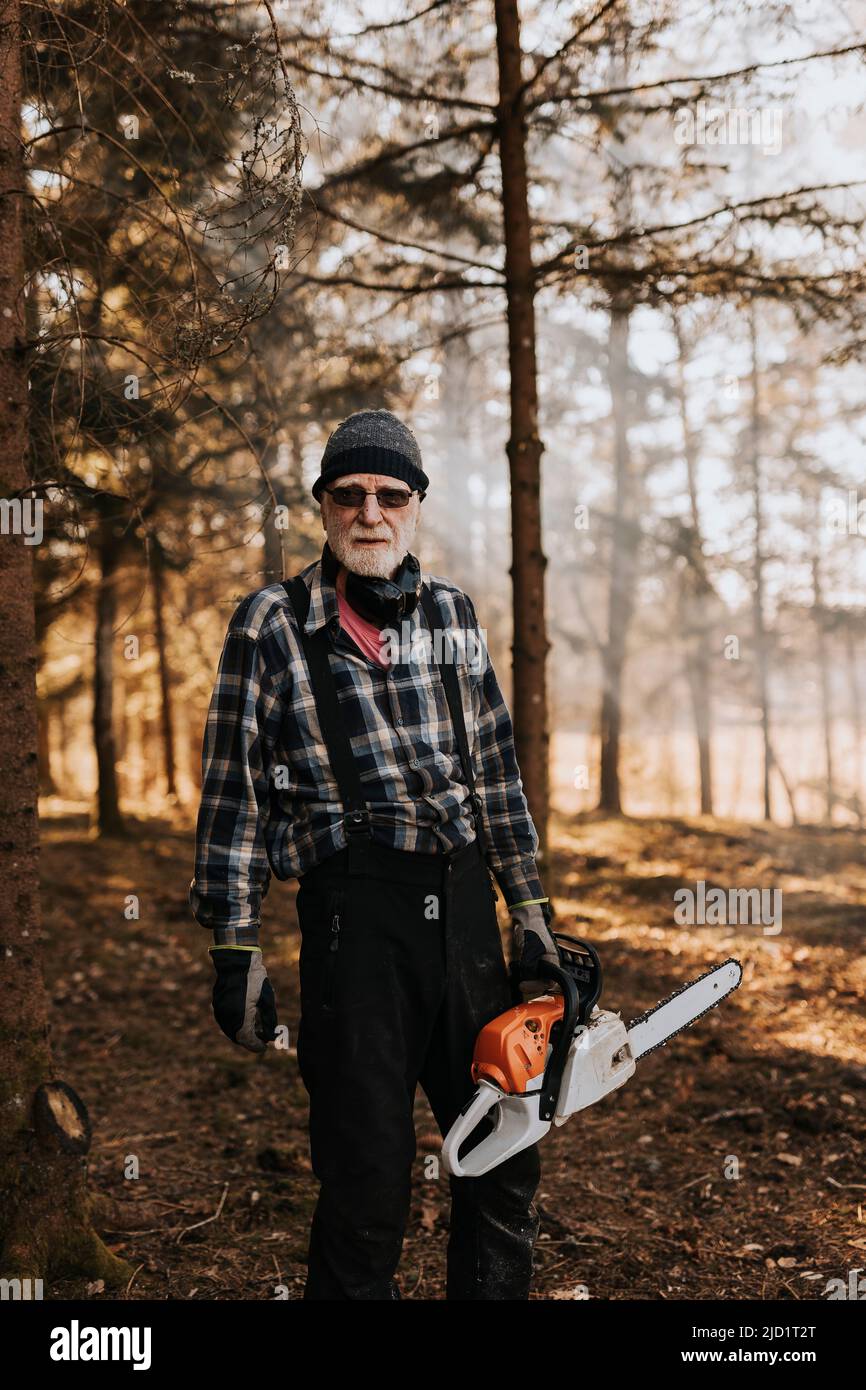 Uomo anziano in legno che tiene motosega Foto Stock
