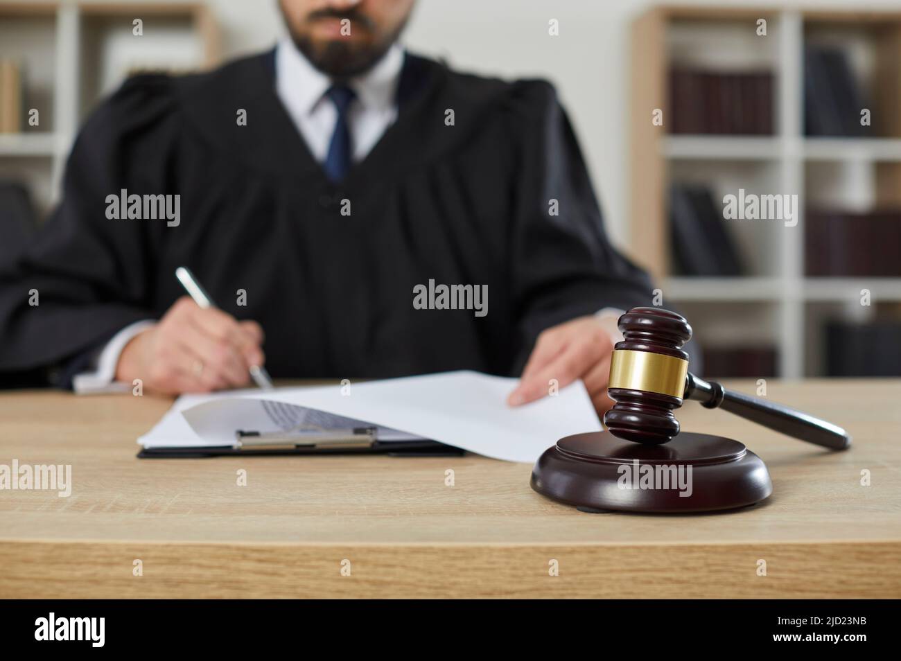 Gavel su un tavolo di legno in tribunale, con un giudice che firma alcuni documenti sullo sfondo Foto Stock