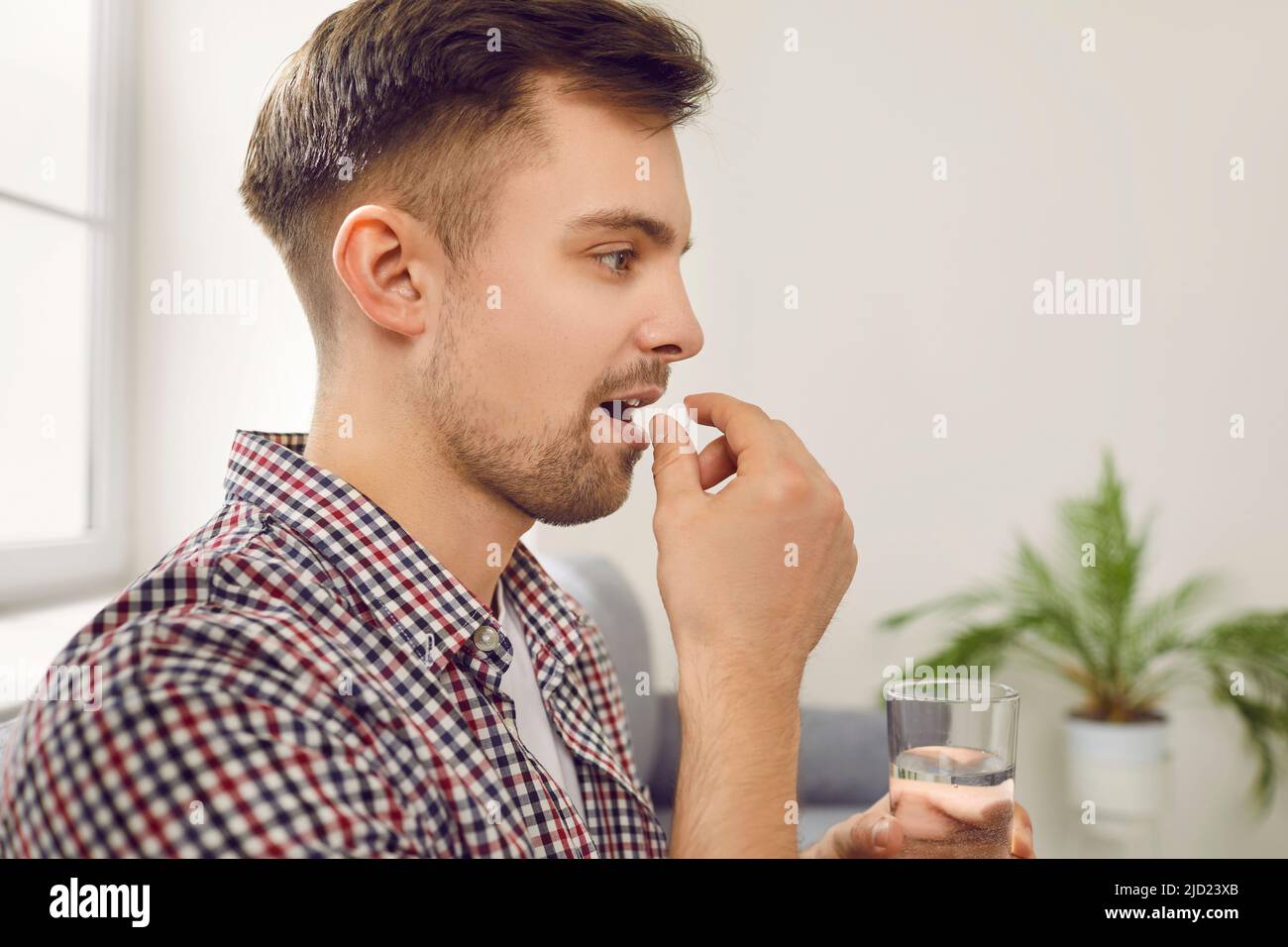 Primo piano di un giovane malato che prende le pillole prescritte e beve un bicchiere d'acqua Foto Stock