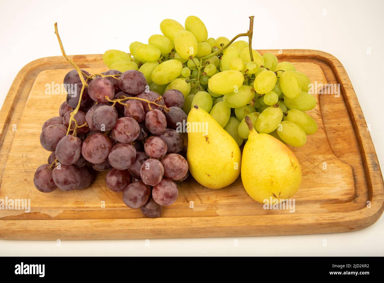 Uve gialle, uve rosse e pere gialle su un tagliere di legno Foto Stock