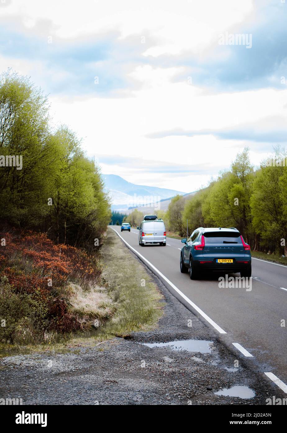 Tre auto in fila su una strada con la montagna in lontananza sull'isola di Skye, Scozia. Foto Stock