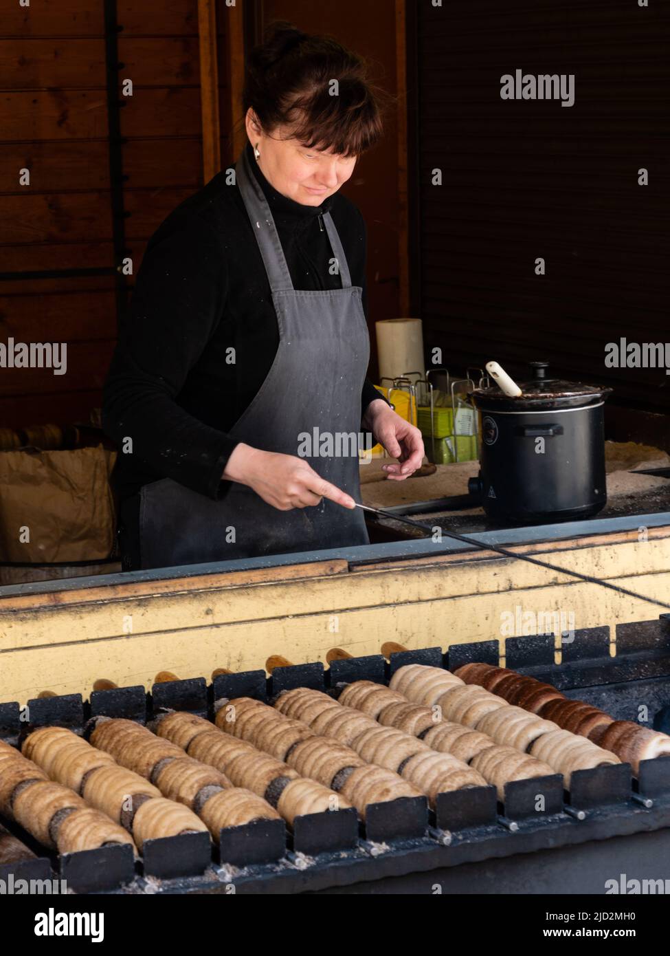 Karlovy Vary, Boemia, Repubblica Ceca - Maggio 28 2022: Donna che cuoce tradizionale Trdelnik Spit Cake su un fuoco di carbone. Foto Stock