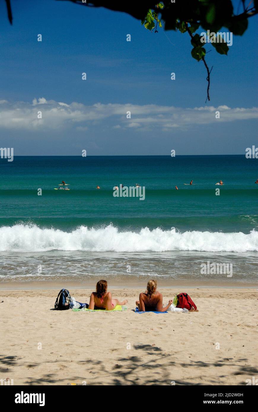 I giovani turisti si crogiolano al sole di Bali mentre guardano i surfisti alla famosa spiaggia di Kuta. Foto Stock