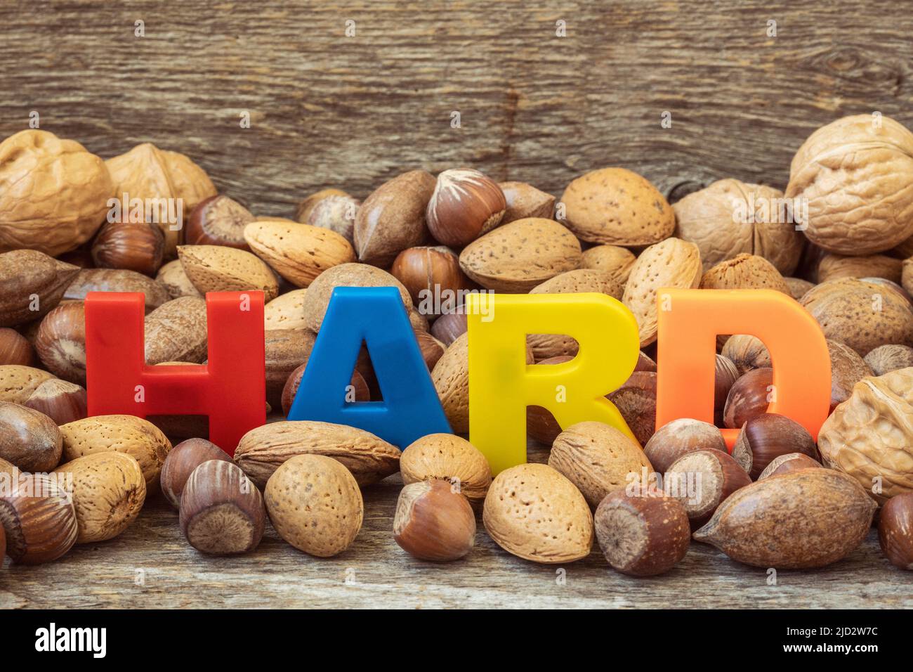 La parola HARD è rivestita con lettere colorate in un mucchio di noci assortite. Immagine concettuale. Foto Stock