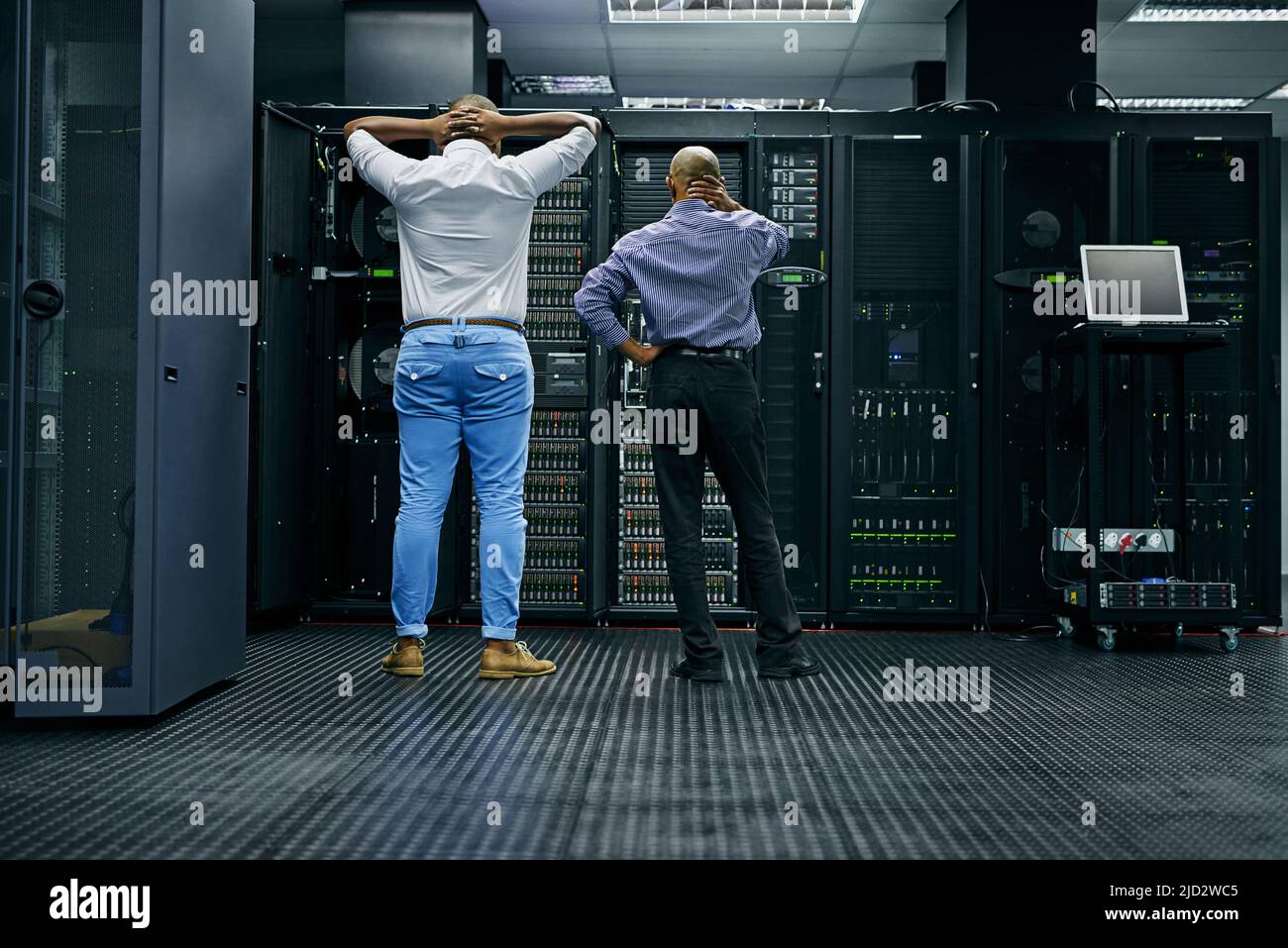 Nel frattempo nella sala server.... Ripresa posteriore di due tecnici IT che hanno difficoltà a riparare un computer in un data center. Foto Stock