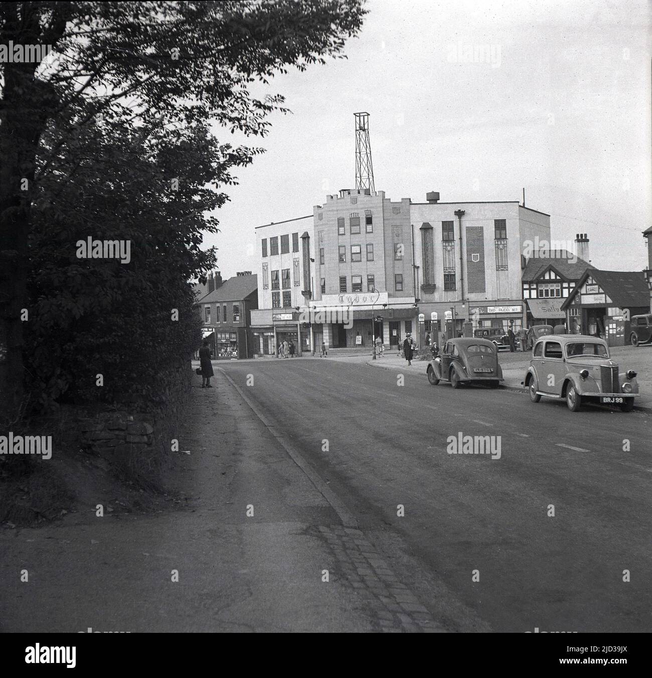 1940, storico, vista a distanza del cinema Tudor a Bramhall, Stockport, Inghilterra, Regno Unito. Situato in un angolo con Woodford Road e Meadway, l'edificio è stato progettato dall'architetto George Clayton, con l'auditorium decorato in stile Tudor e aperto il 31st marzo 1935 con Clark Gable in "IT Happen One Night". Questa foto, scattata nel 1940, ha visto il film 'Dad Rudd MP' essere mostrato. Le auto dell'epoca possono essere viste parcheggiate sulla strada. Foto Stock