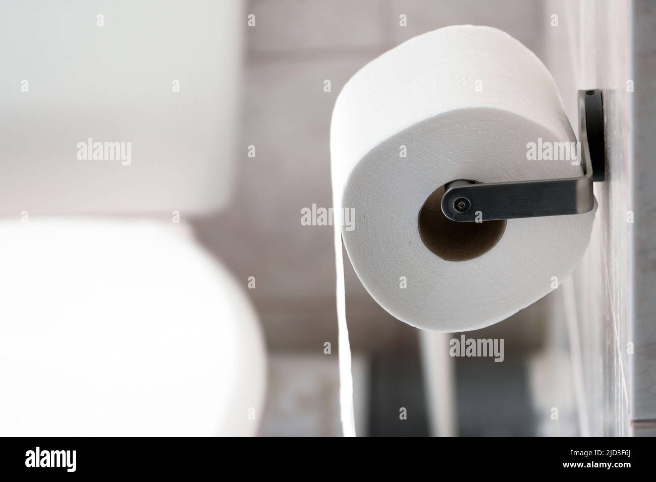 Rotolo di carta igienica appeso a un supporto metallico sulla parete del bagno. Foto Stock