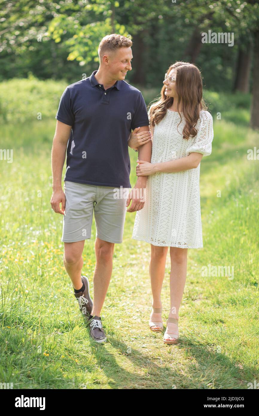 Scatto all'aperto di una giovane coppia innamorata camminando su strada attraverso il campo di erba. L'uomo e la donna sono felici insieme Foto Stock