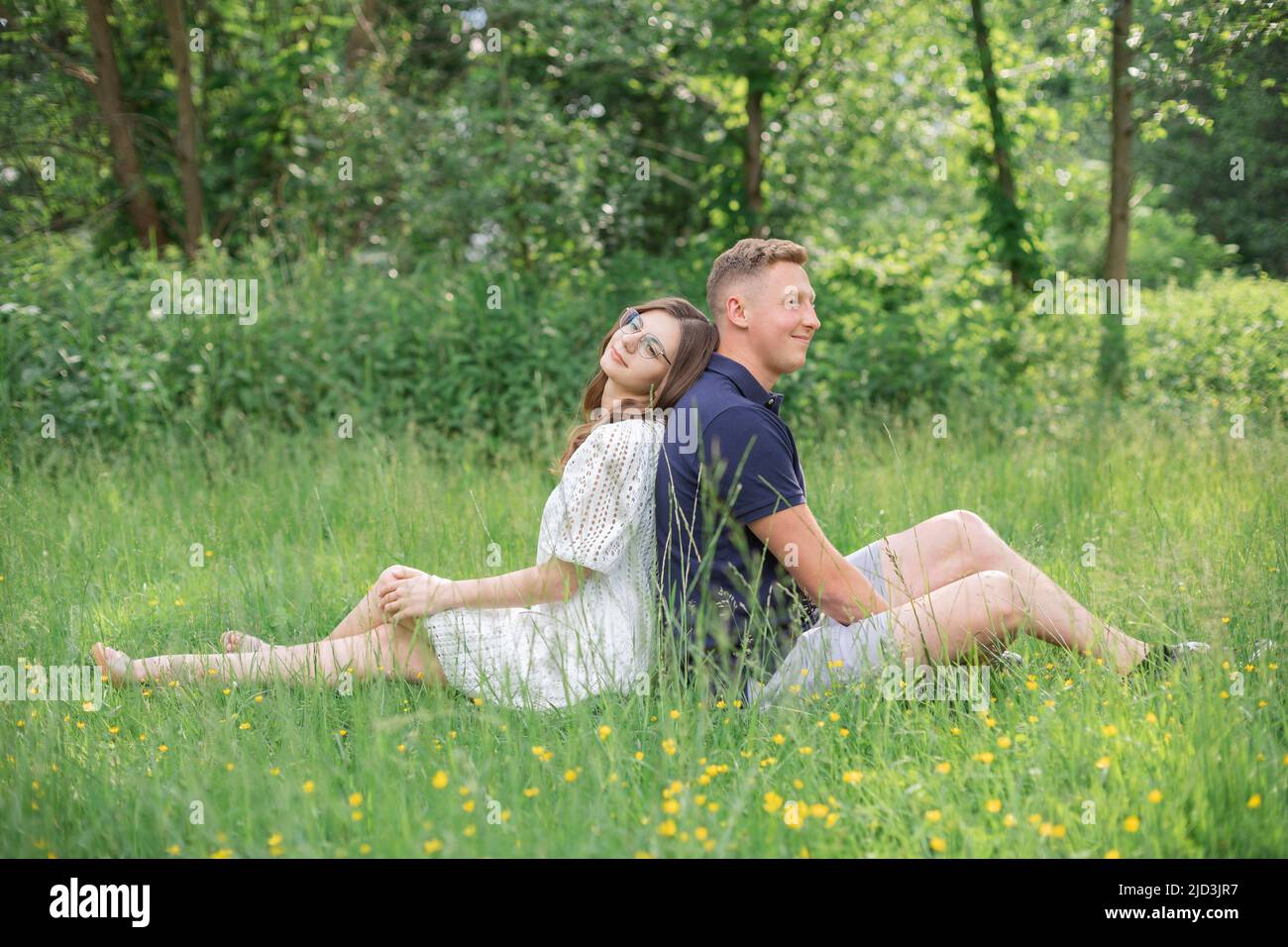 Giovane coppia affettuosa seduta sull'erba nel parco, ritorno a schiena. Giovane uomo e donna che si godono giorno d'estate. Gente felice nell'amore, luna di miele Foto Stock