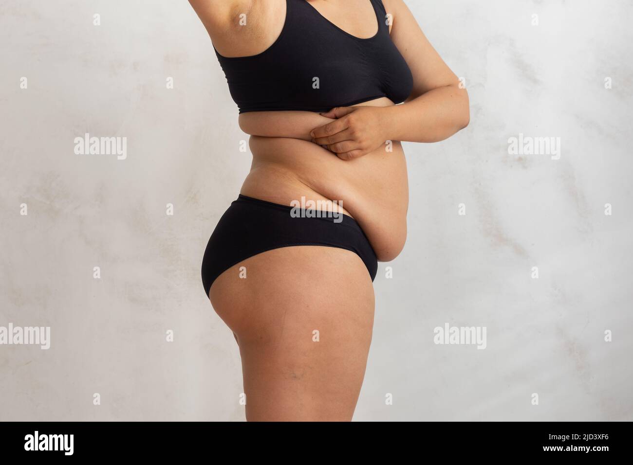 Cropped donna grasso sovrappeso pizzicando e controllando il volume dei lati in bikini nero. Problema cutaneo in eccesso dopo il parto Foto Stock