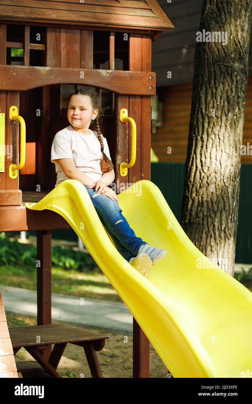 Carina bambina che scende lo scivolo giallo nel parco giochi per bambini. Vacanze estive in campeggio, centro turistico. Passeggiate e giochi all'aperto, sport Foto Stock