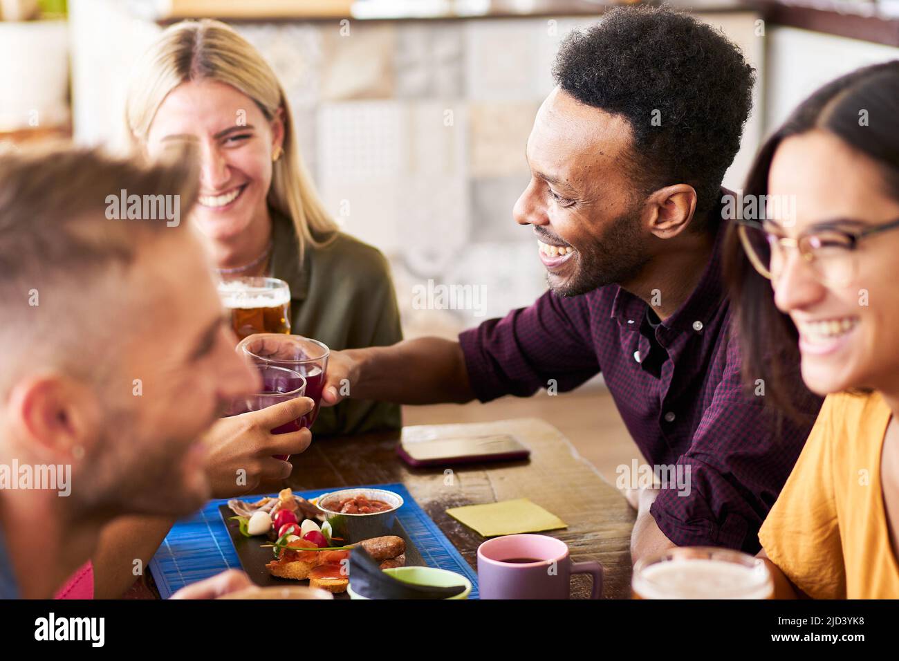 Gruppo di simpatici multiculturali bevono birra in un bar. 30s giovani amici divertirsi e pranzare e bere alcolici in un happy hour sul tetto. Foto Stock