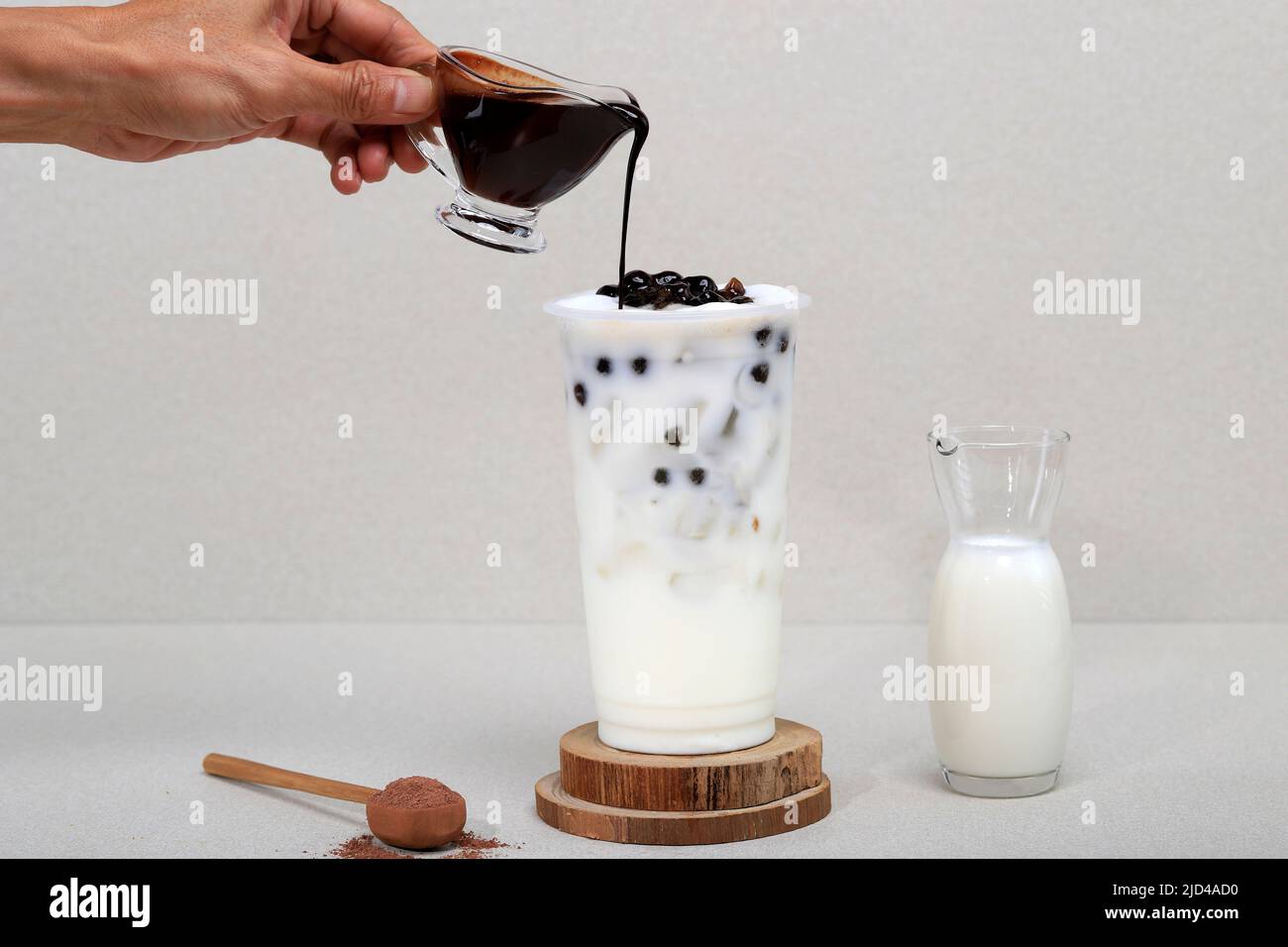 Versare il liquido di zucchero di palma sul tè del latte di Boba con in un Tall Glass con ghiaccio su un tavolo di pietra grigia Foto Stock