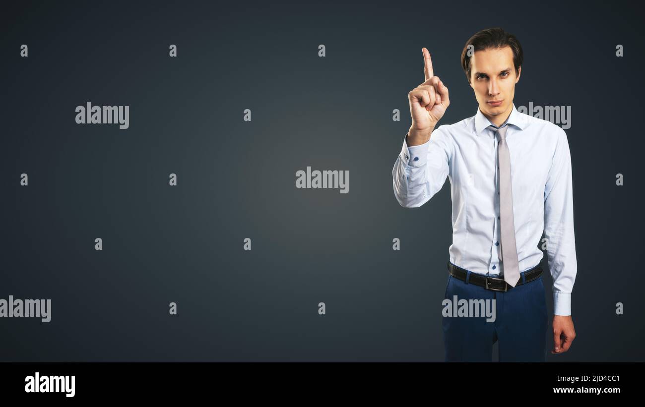 Giovane uomo bello in camicia con alzarsi la mano e l'indice isolato su sfondo astratto scuro con posto vuoto per il tuo logo o testo, mock up Foto Stock