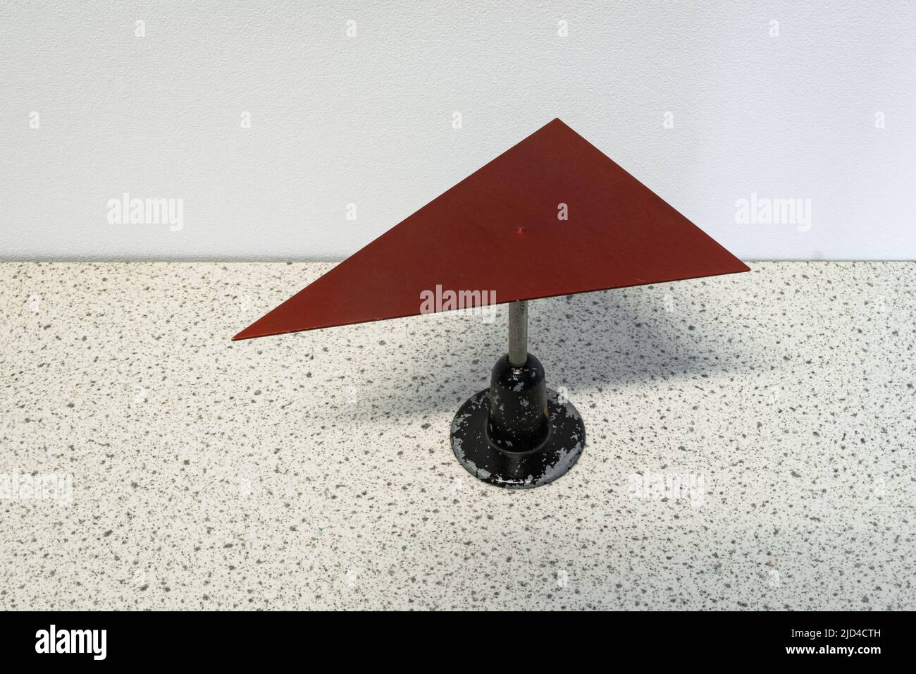 Esperimento di fisica in cui una piastra metallica triangolare rossa si sta equilibrando su un ago. Il baricentro della piastra è posizionato esattamente sulla parte superiore dell'ago. Foto Stock