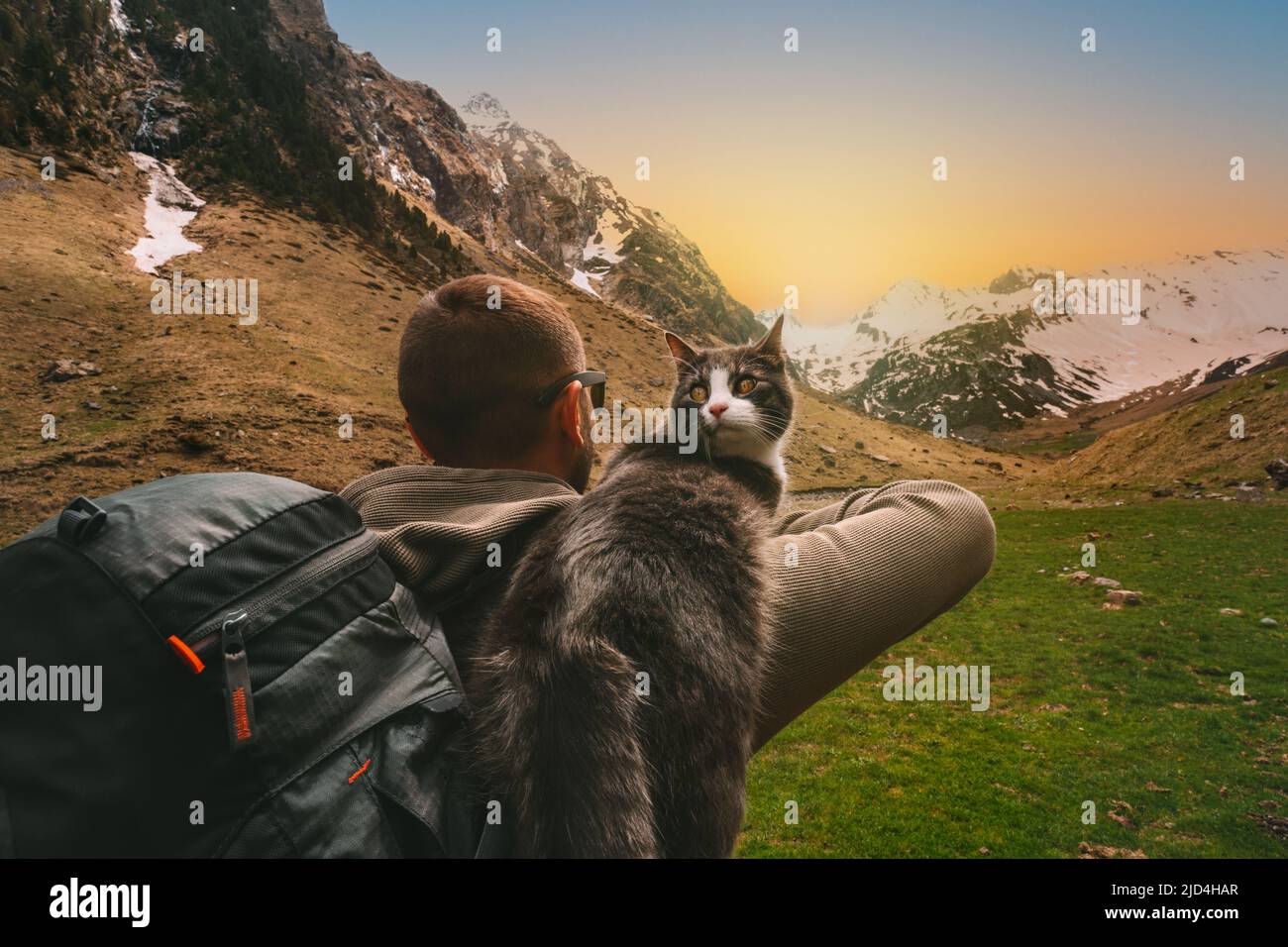 Uomo che cammina all'aperto in montagna con il suo amico gatto sulla spalla. Scena nella natura al tramonto. Uomo che passa il tempo con il suo animale domestico. Momenti di vita migliori Foto Stock