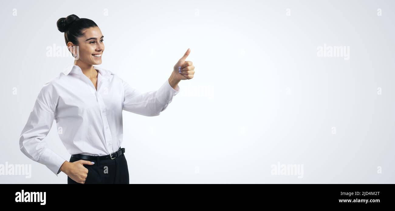 Come concetto con ragazza felice in camicia bianca tenendo i pollici su sfondo grigio chiaro parete con spazio vuoto per voi testo, mockup Foto Stock