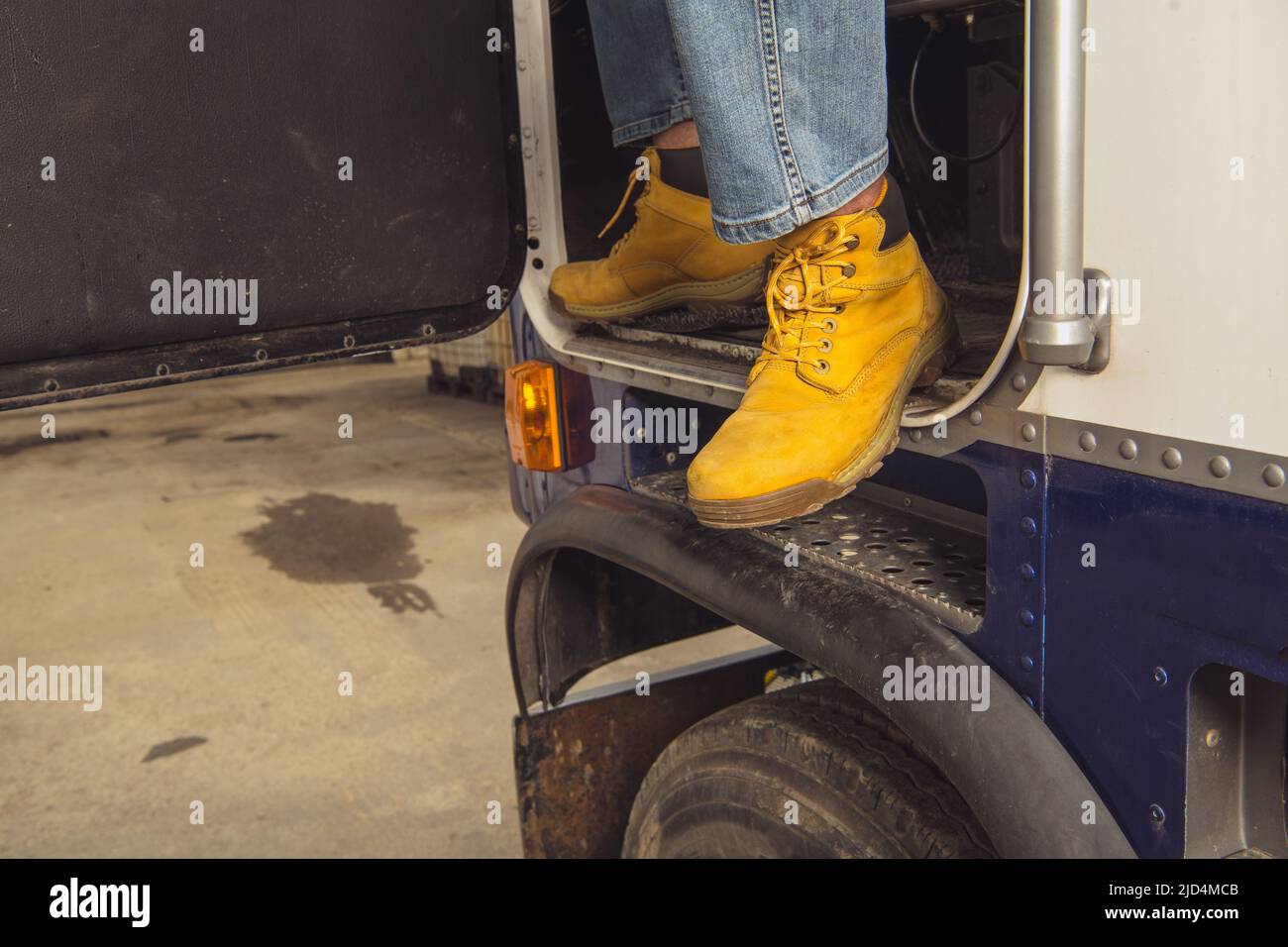 Primo piano delle gambe del trucker in stivali arancioni che escono dal camion dopo aver completato con successo un percorso. La fine del lavoro. Tema trasporti. Foto Stock