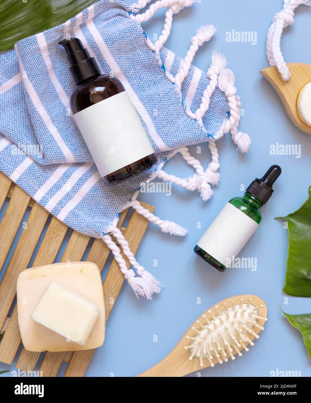 Dispenser in vetro con una pompa, accessori per la cura della pelle e dei capelli su telo da bagno blu vista dall'alto, spazio per la copia. Mockup di imballaggio. Prodotti naturali fatti in casa Foto Stock