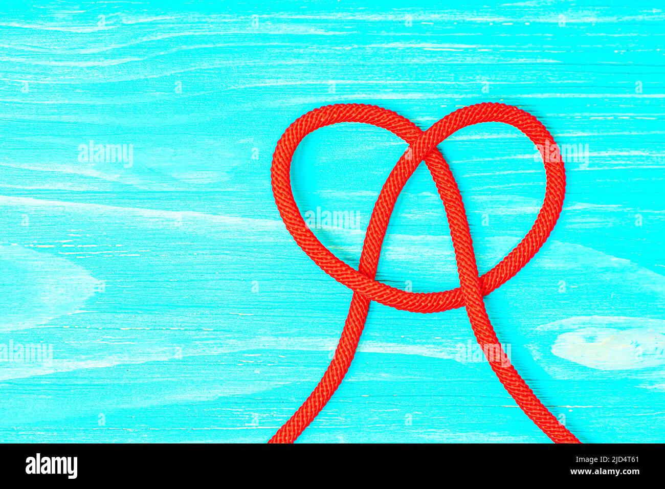 Cavo intrecciato rosso legato a forma di cuore su sfondo di legno blu con spazio copia. Foto Stock