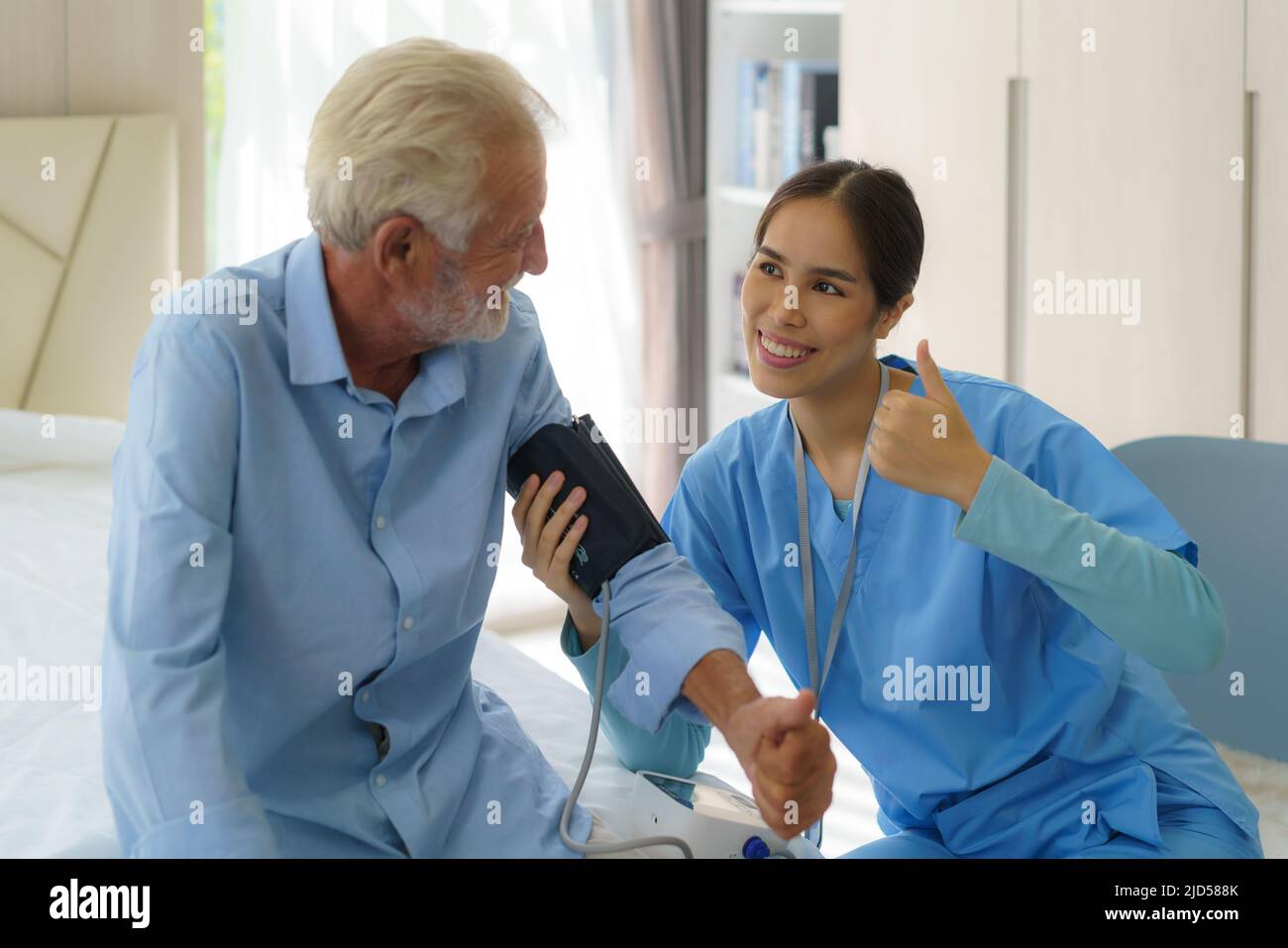 Asian attento operatore sanitario utilizzando il tonometro mentre l'anziano ha problemi di respiro. Medico femminile che misura la pressione sanguigna dell'uomo anziano a casa. Foto Stock
