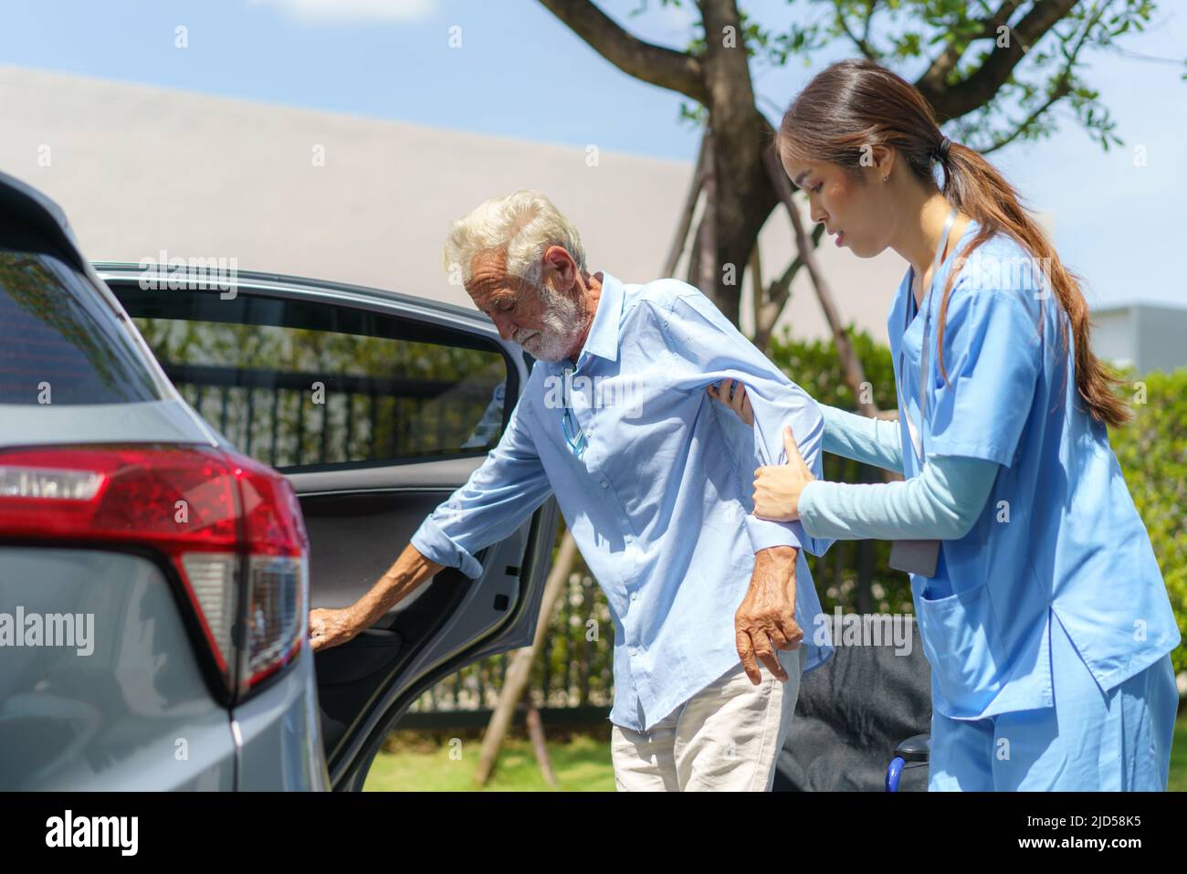 Giovane donna asiatica donatrice di cure infermieristiche aiutando anziani disabili in auto in fornt di casa. Foto Stock