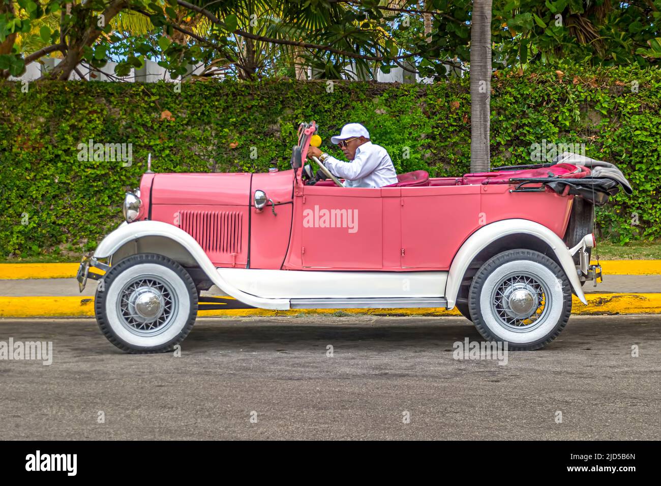 Un autista si siede nella sua bella auto d'epoca rosa fuori dall'Hotel Nacional de Cuba a l'Avana, Cuba Foto Stock