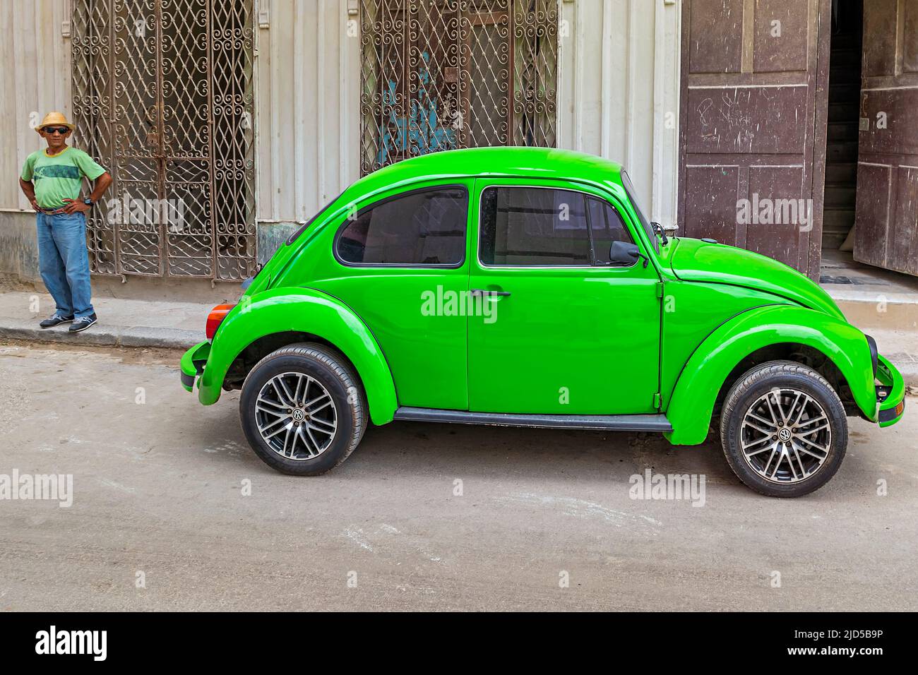 Verde brillante Vintage Volkswagen Beetle e uomo cubano in verde T-shirt nelle strade di Old Havana, Cuba Foto Stock